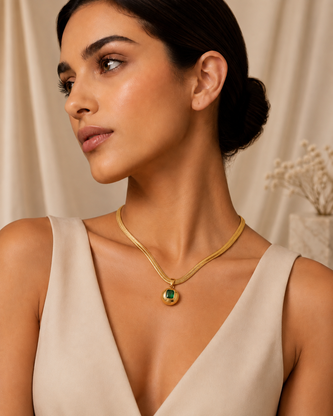 Model wearing gold herringbone necklace with emerald pendant