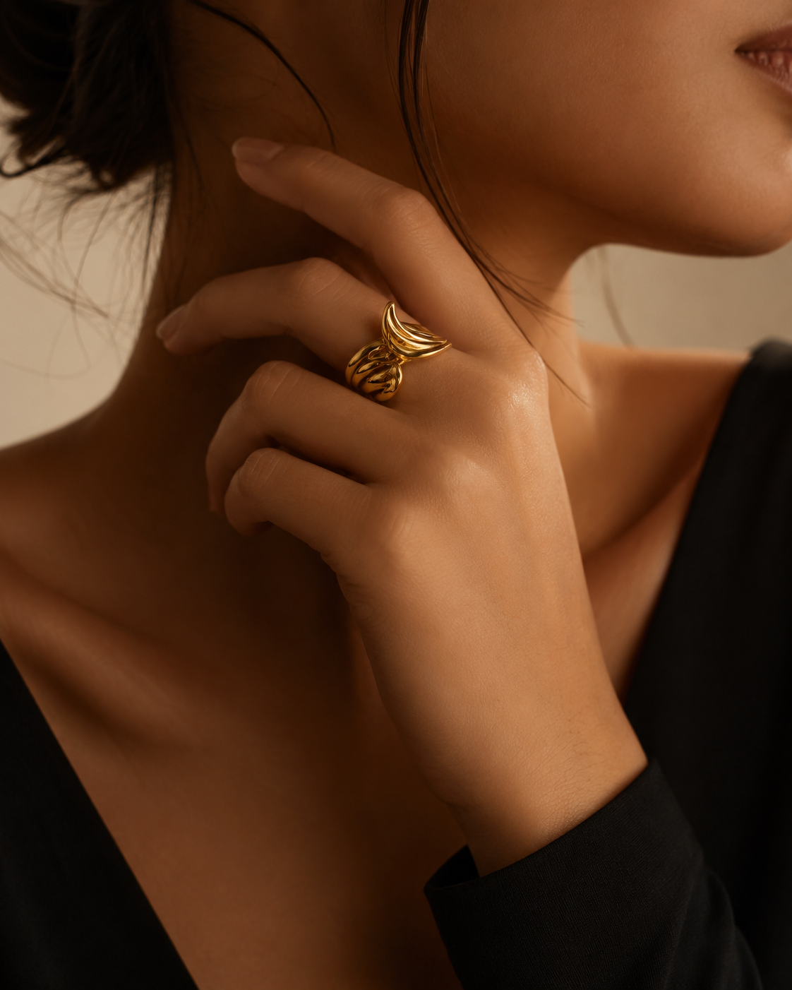 Model wearing sculptural gold ring, close crop on hand and neck